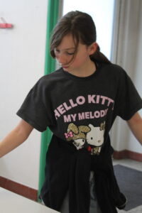 Girl wearing a dark Hello Kitty My Melody T-shirt standing in a hallway, with a jacket tied around her waist.