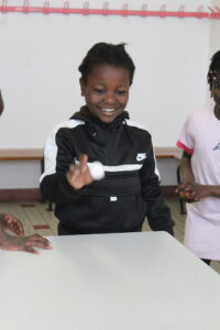 Child in a black Nike hoodie smiles as they toss a small white ball onto a table indoors.]"Seems extra quote; fix