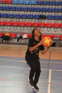 Young boy in a black shirt leaps in a gym, holding an orange basketball and looking up for a shot.