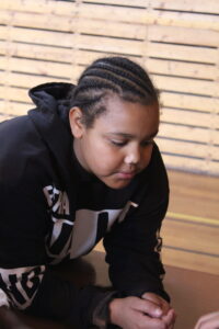 A young person with cornrow braids wearing a black hoodie, looking down at their hands.